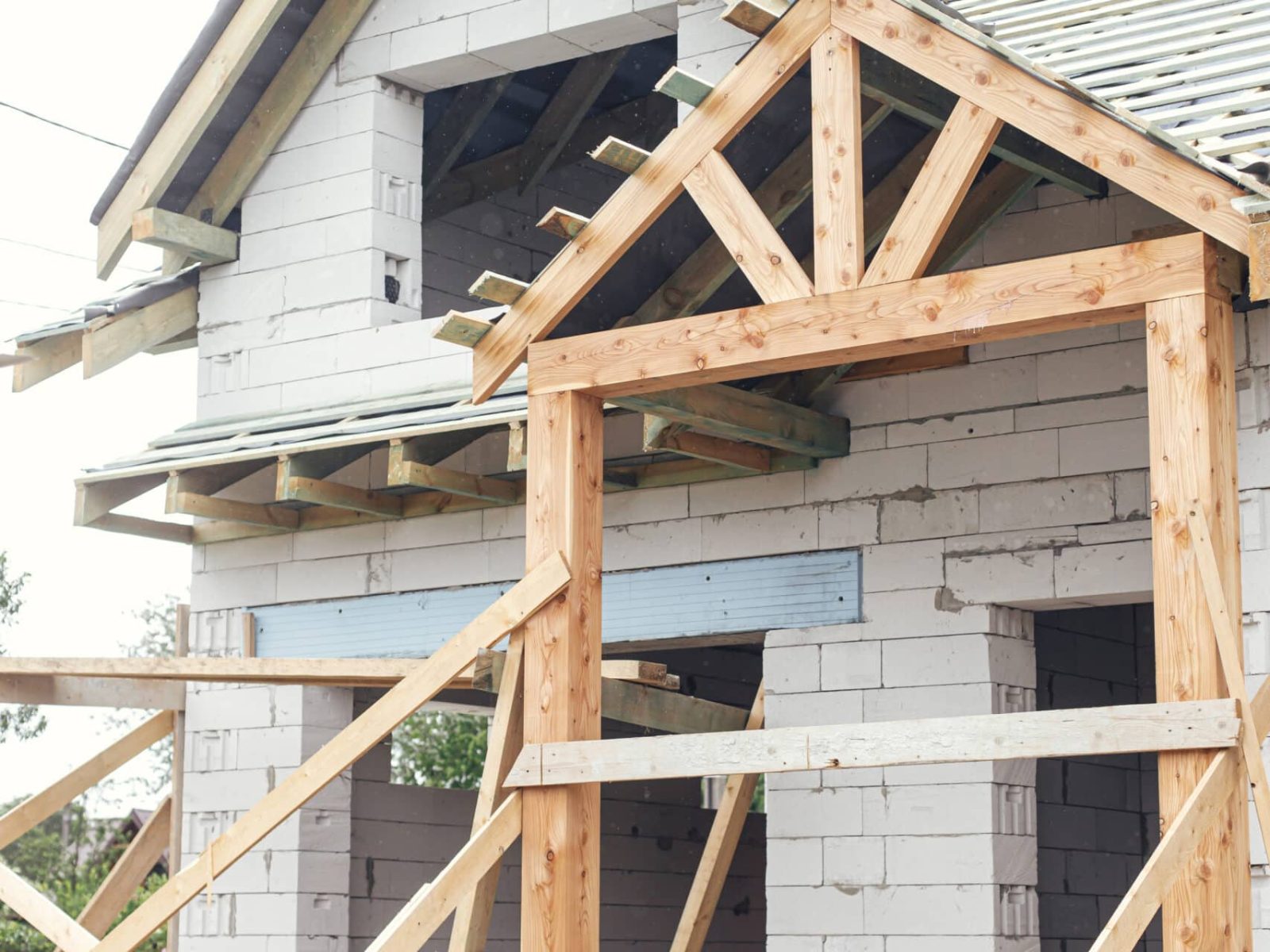 Unfinished house. Wooden roof framing with vapor barrier and dormer on block walls with windows. New modern farmhouse construction. Timber trusses Rafters and beams on aerated concrete blocks